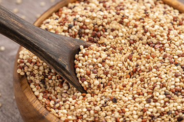 Mix of white, red and black quinoa seeds - Chenopodium quinoa. Top view of a wooden bowl filled with mixed quinoa grains and a wooden spoon, featuring white, red, and black quinoa, perfect for health 