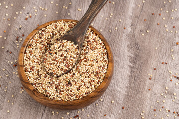Mix of white, red and black quinoa seeds - Chenopodium quinoa. Top view of a wooden bowl filled with mixed quinoa grains and a wooden spoon, featuring white, red, and black quinoa, perfect for health 