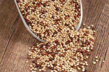 Close-up of mixed quinoa grains spilling from a metal scoop onto a wooden surface, featuring red,...