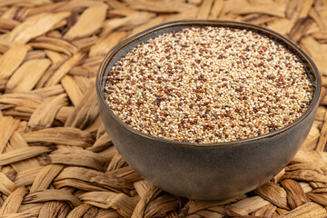 Bowl filled with mixed quinoa grains placed on a woven rustic surface, featuring red, white, and black quinoa seeds. Ideal for healthy food and nutrition projects.