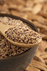 Mixed quinoa grains in a wooden spoon resting on a bowl filled with quinoa seeds, featuring red, white, and black quinoa. Perfect for healthy food and nutrition themes.
