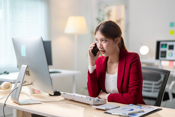 Obraz premium A woman in a red jacket is talking on her cell phone while sitting at a desk