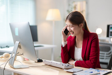Obraz premium A woman in a red jacket is talking on her cell phone while sitting at a desk