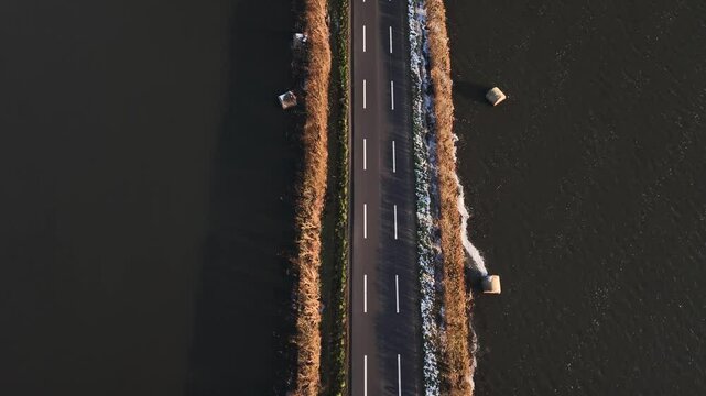 A drone view of a long road traversing the marshes in Normandy on a sunny day,