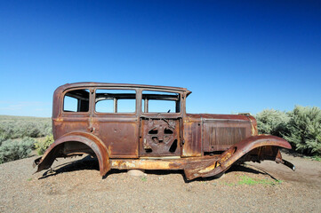 Fototapeta premium A rusted vintage car body abandoned in a desert landscape under a clear blue sky, symbolizing decay, history, and the passage of time in the American Southwest