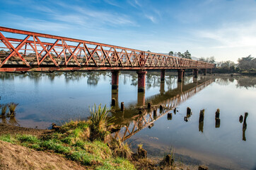 The river Taieri at sunrise where it becomes an estuary and the Historic Henley suspension bridge...