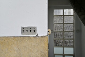 The industrial-style stainless steel switch is mounted on a textured wall, next to a wooden-framed glass door that offers a view of a grey tiled rooftop.