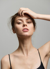Fototapeta premium Confident young woman with tousled hair striking a pose. She wears a simple black top, showcasing natural beauty against a soft grey background.