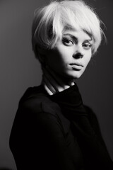 Elegant young woman with short blonde hair in black outfit, showcasing a contemplative expression against a soft gradient background. Fashion and beauty concept.