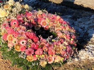 Großer runder Trauerkranz  mit bunten Blumen nach Beerdigung auf dem Friedhof im Winter bei Frost 