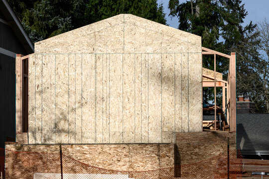 Large addition to residential house, construction in progress at framing stage with OSB, Oriented Strand Board, exterior wall installed on south end, sunny winter day job site
