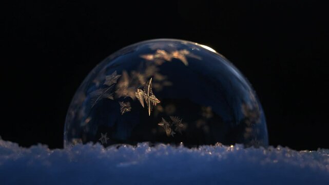 Soap bubble on snow freezing in cold winter on black background