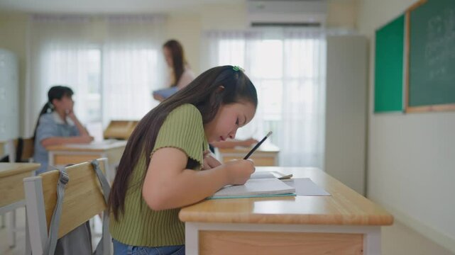 Adorable student girl writing a book in classroom at elementary school. 