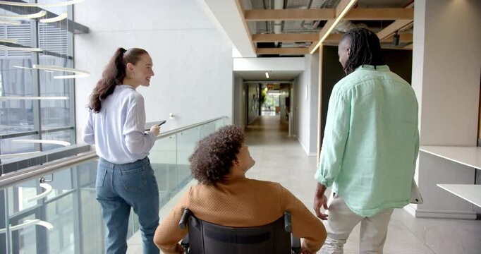 Colleagues in office hallway, man in wheelchair discussing with coworkers