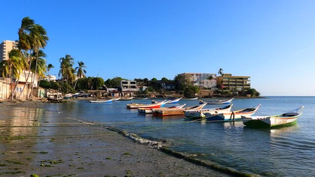 As the sun sets over Playa Pampatar in Isla Margarita, Venezuela, fishing boats are moored in a tropical bay. The golden light, palm trees, and vivid Caribbean hues create a serene coastal scene.