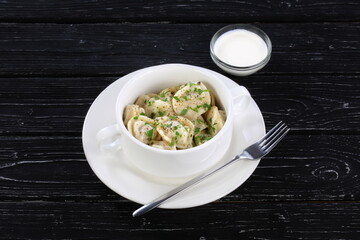 Dumplings with sour cream on a black wooden background