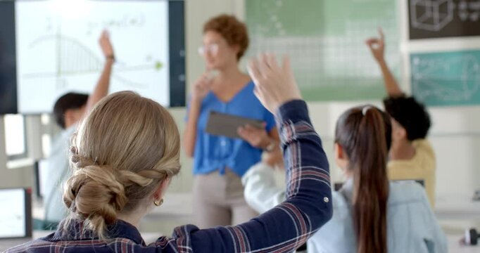 In high school, students raising hands to answer teacher's question in classroom