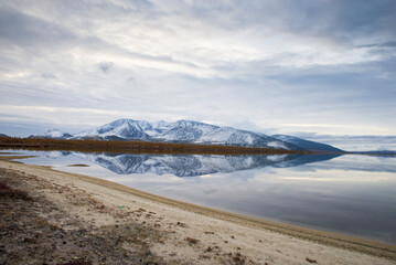 Russia. Magadan Region. Beautiful Lake Momontay against the backdrop of a snowy mountain range. Late autumn in the vicinity of Lake Momontay.