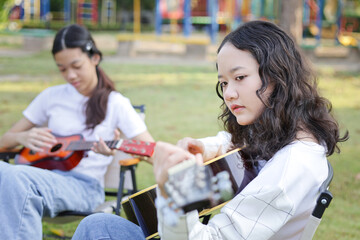 Asian girls playing guitar in outdoor setting, Friends playing guitar on picnic in park