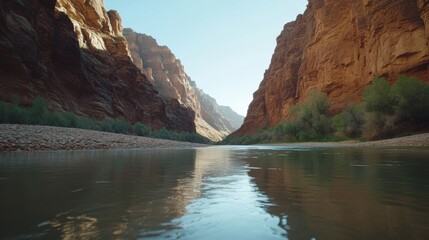Calm river flows through a narrow canyon, reflecting sunlight, with towering red rock walls and riparian vegetation, ideal for travel brochures