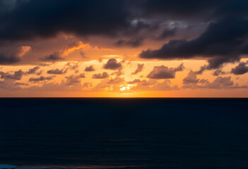 Obraz premium Dramatic sunset over ocean, Vibrant orange and gold sky, Dark stormy clouds, Calm sea reflections, Moody seascape, Twilight horizon, Atmospheric cloudscape, Serene coastal scene, Rich color palette, 