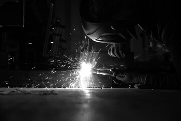a person wearing a welding mask works on metal with a welding torch, creating sparks through the...