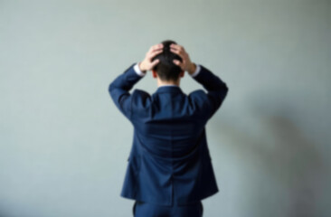 blur background of Rear view of business man standing in front of a wall hands on head wondering what to do next. Full length of businessman facing the wall 