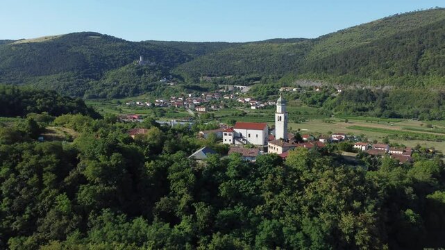 Aerial view of the Church of St. Anton in a scenic valley with Rihemberk Castle visible on a hill in the background, Slovenia.