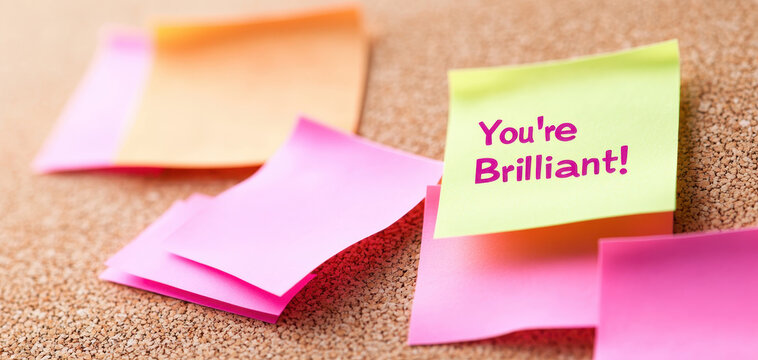 You Brilliant Bright post it notes with compliments on corkboard create uplifting atmosphere. Perfect for motivation and encouragement in any workspace