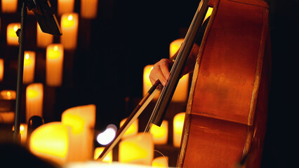 Close-up of a double bass being played on a stage with lit candles. The background is blurred and orange. Candlelight concert.