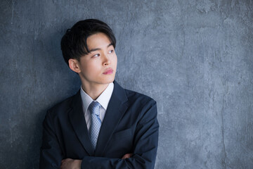 濃いグレーバックの背景にスーツで立つ20代の若い男性の見上げる