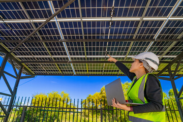 Engineer in safety vest and helmet pointing towards a solar powered carport, illustrating...