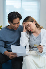 Fototapeta premium Young asian couple feeling stressed and frustrated while managing home finances, reviewing expensive bills and having financial problems, sitting on the sofa at home