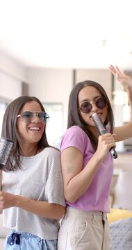 Vertical video: Singing and having fun, two teenage girls using hairbrushes as microphones