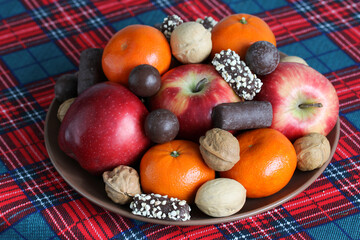 Plate presenting assorted fruits, nuts, and chocolates on plaid tablecloth