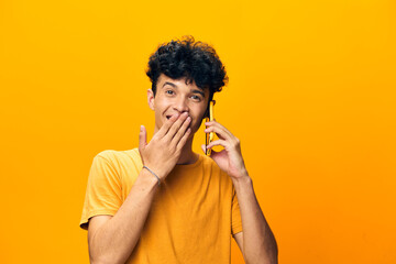 Young man smiling while talking on the phone, wearing a yellow t shirt against a bright yellow background, conveying happiness and joy Perfect for communication themes