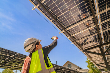 Engineer inspecting solar panels under a solar-powered carport on a sunny day, ensuring optimal...