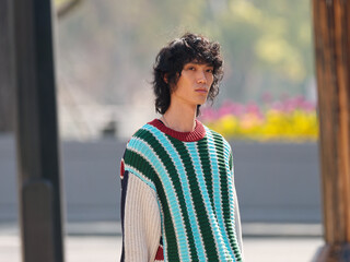 Portrait of handsome Chinese young man with striped sweater walking in the street, young guy with black curly hair with urban background. male fashion, cool Asian young man lifestyle.