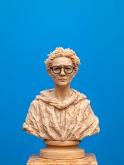 Obraz premium Wooden Bust of a Contemplative Figure with Glasses Against a Blue Background