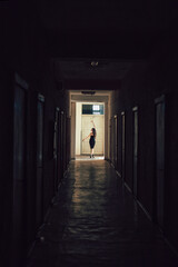 a long dark corridor with doors on both sides. At the end of the corridor, in the bright doorway, there is a girl standing.