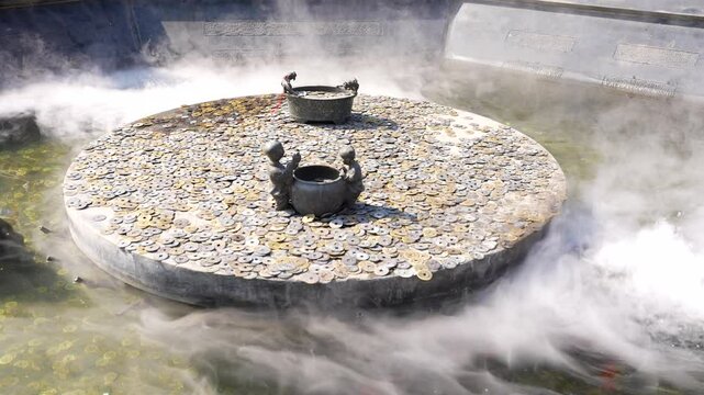 Buddhist pond with a stone wheel covered by coins with nebulization