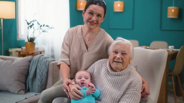Portrait of a three-generation family, 80s grandmother, mature mother, and newborn baby smiling and looking at the camera at home in the living room
