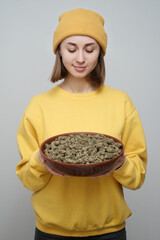 Young woman in yellow holding a bowl of dried cannabis buds