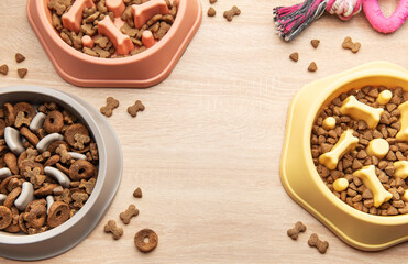 Different dry dog food in slow feeder bowls and toy on wooden table