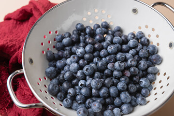 Close-up of fresh blueberries in a white colander with red cloth and light background. Concept of natural cooking and healthy eating