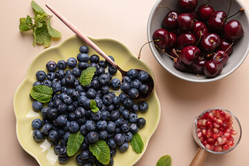 Fresh fruits: blueberries, cherries and pomegranate in plates and cups with mint leaves on light background. Vibrant colors and naturalness. Healthy diet concept