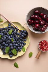 Selection of fresh fruits: blueberries, cherries and pomegranate, presented with mint leaves on beige background. Highlights freshness and vitality. Natural food concept