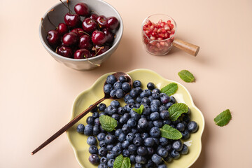 Fresh fruits in containers with mint leaves: green plate with blueberries, bowl with cherries and container with pomegranate. Healthy eating concept