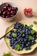 Blueberries, cherries and pomegranates on plate and containers, on light background and decorated with mint leaves. Natural cooking and healthy eating concept