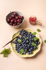 Blueberries, cherries and pomegranate in containers on beige background, decorated with mint leaves, highlighting freshness and vibrant colors. Healthy eating concept